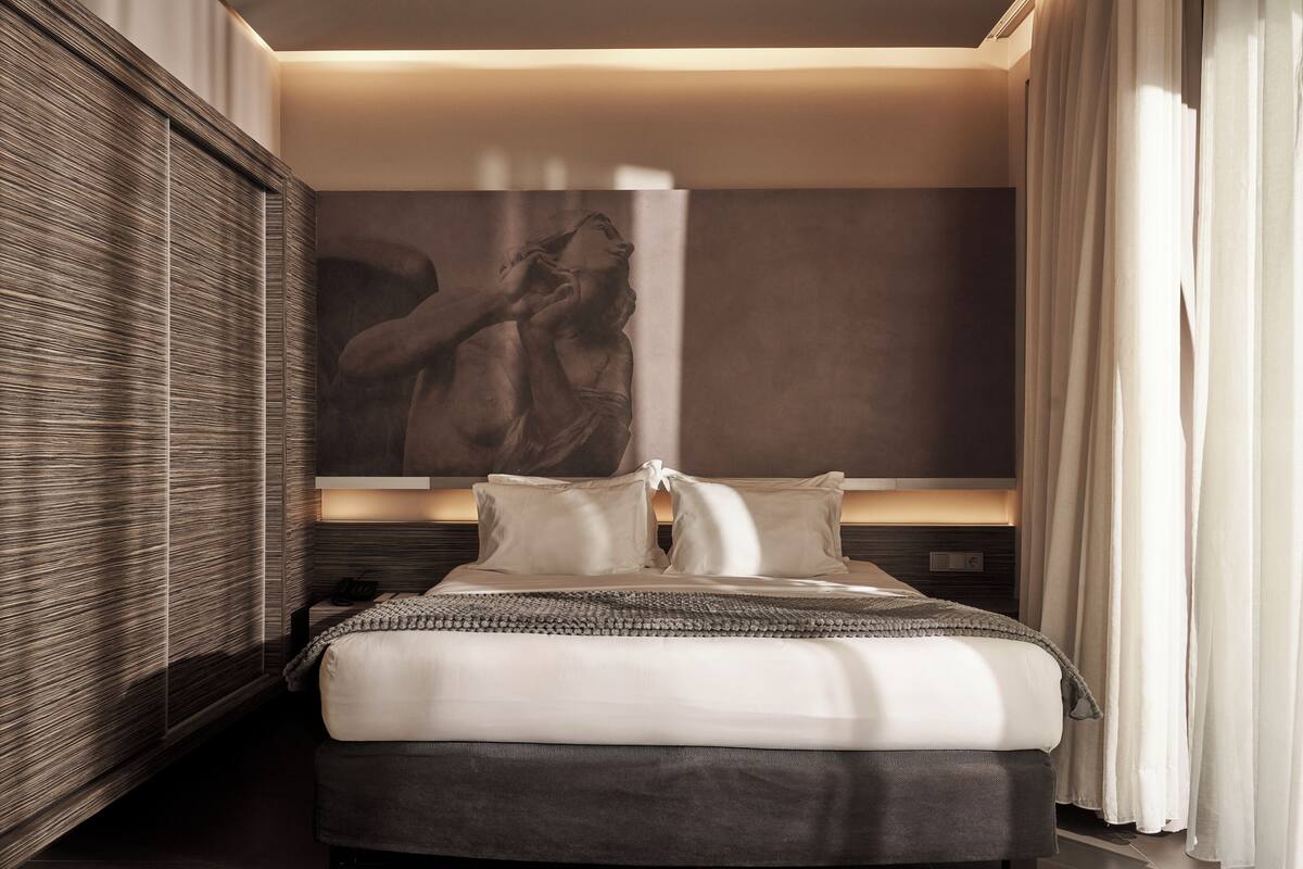 A modern hotel room with a large bed, a wall-mounted artwork, and a bedside table.