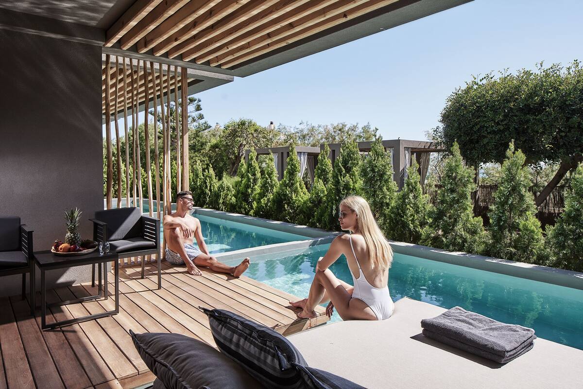 A poolside area with wooden decking, lounge chairs, and a table with fruits.