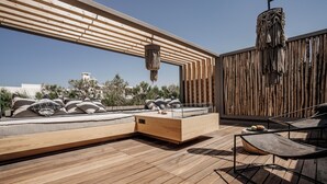 A modern outdoor deck with wooden flooring, a seating area with cushions, a hanging light fixture, and a view of the cityscape.