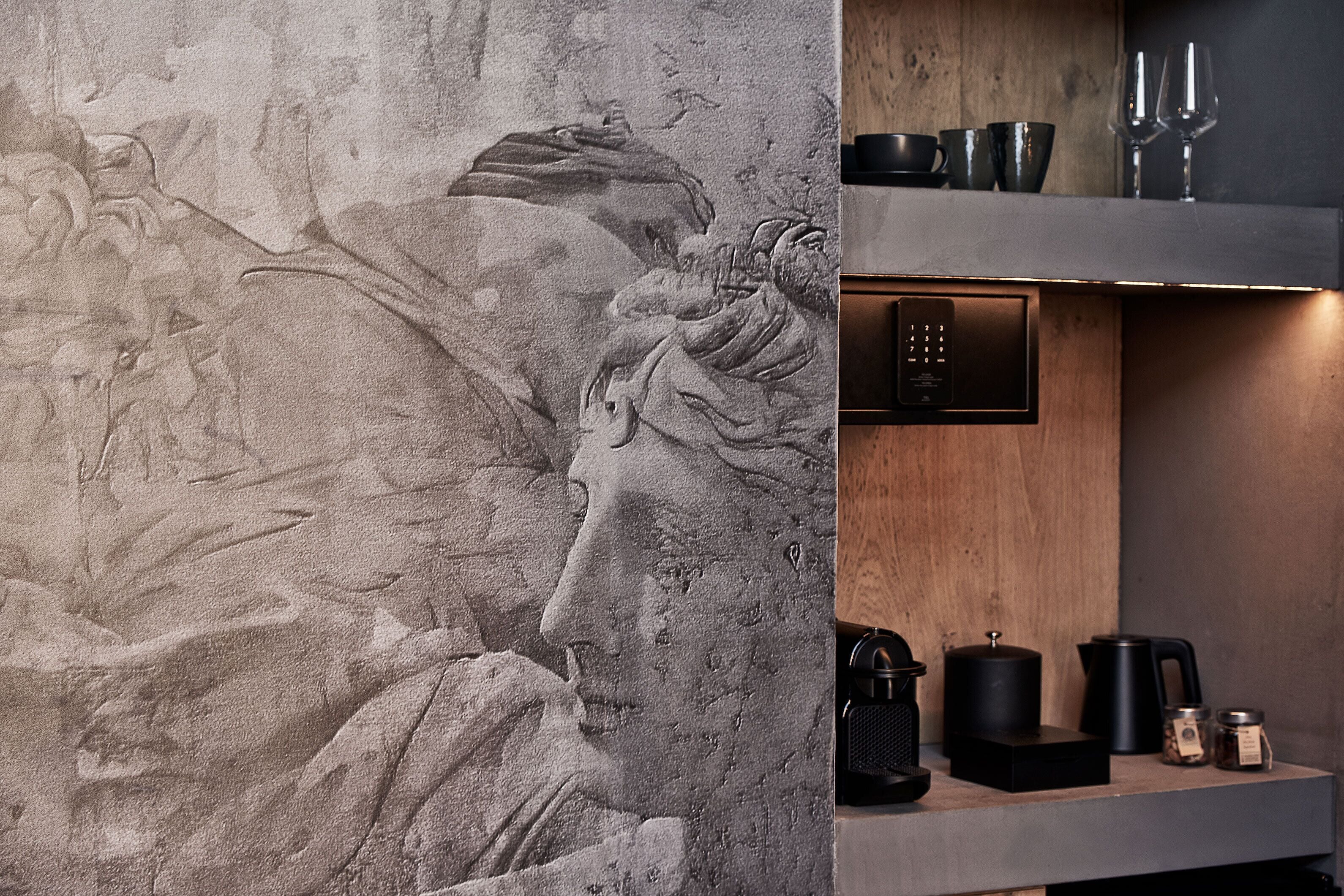 A modern kitchen with a stone wall featuring a relief sculpture, a built-in oven, and a coffee machine.