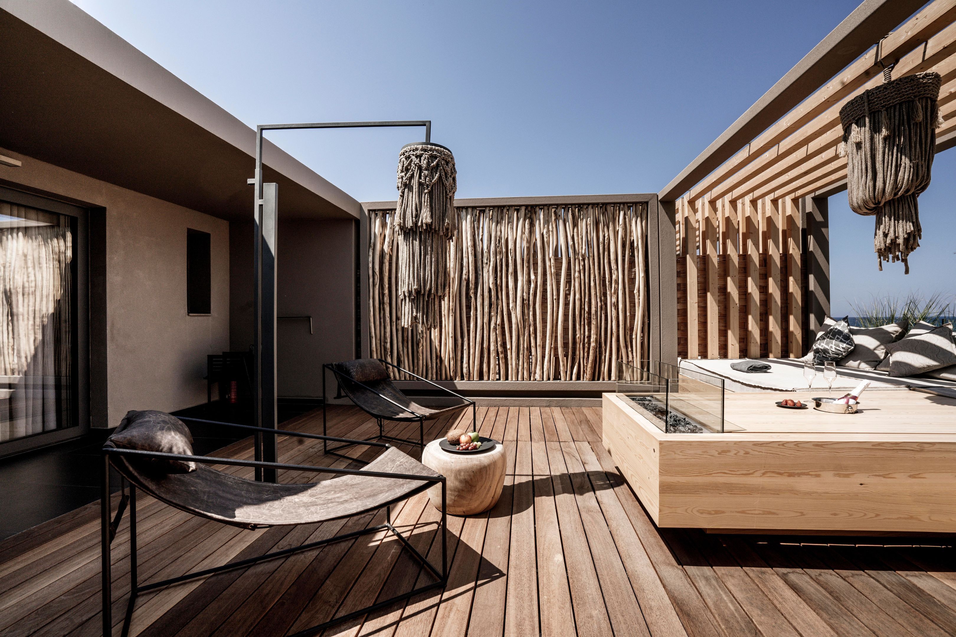 Una terraza moderna al aire libre con piso de madera, una silla de descanso, un reposapiés redondo y un espacio de estar con cojines y una mesita.