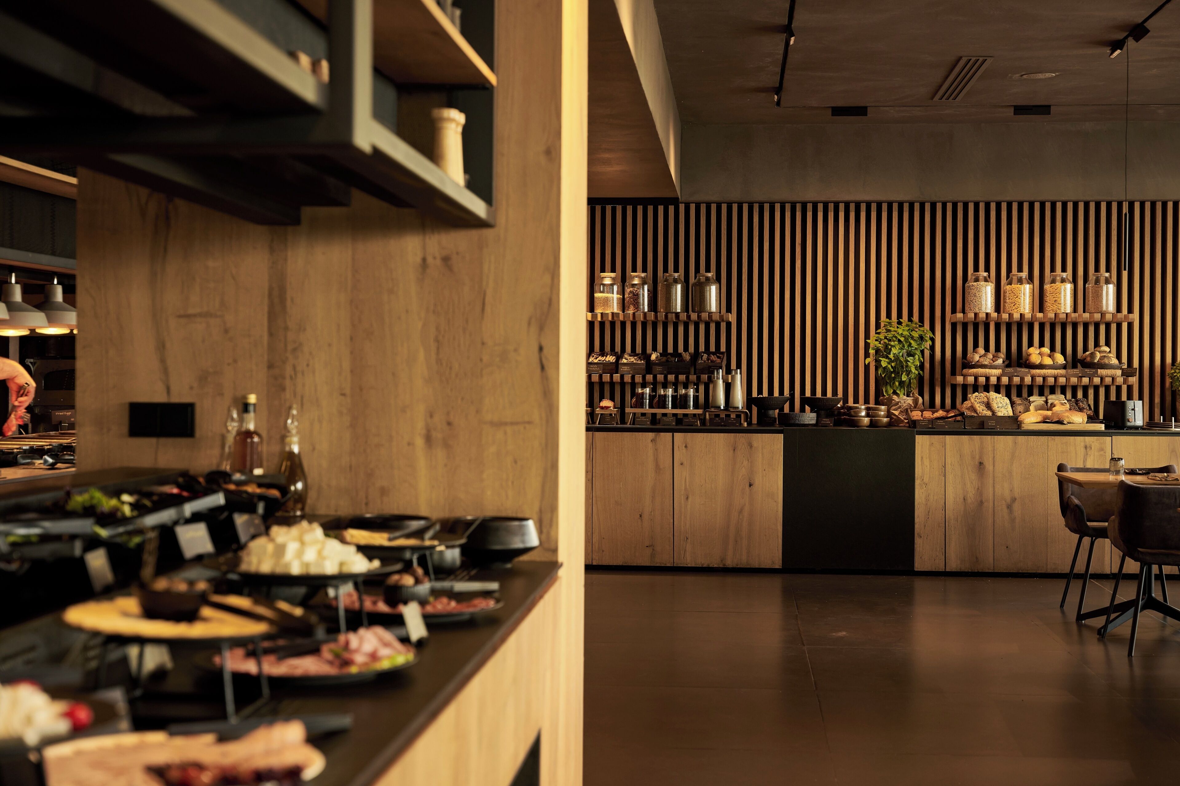 A modern kitchen with wooden cabinetry, a central island, and a variety of food items displayed on shelves.