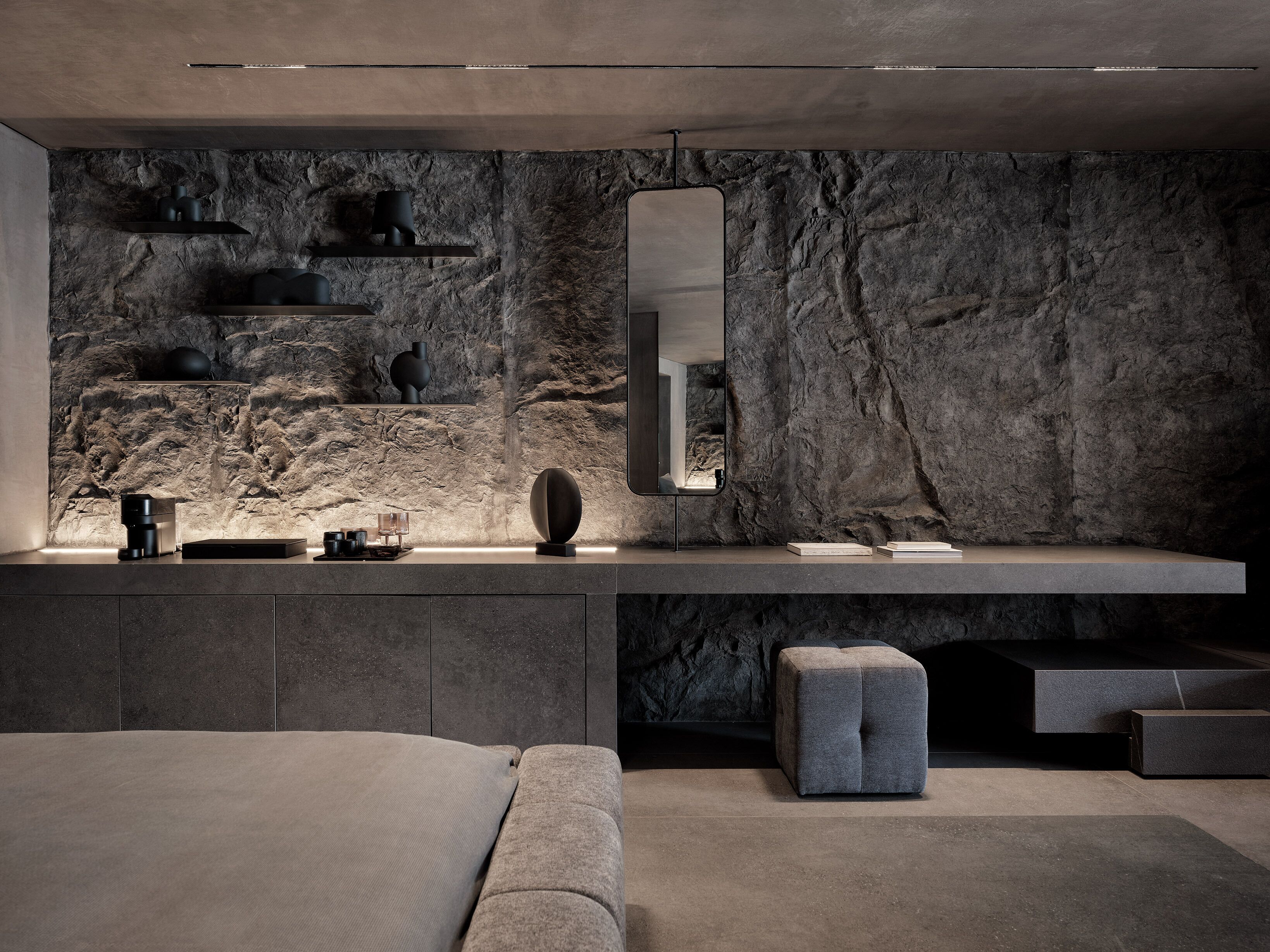 A modern interior with a stone wall, a minimalist desk, and a bed with a grey upholstered headboard.