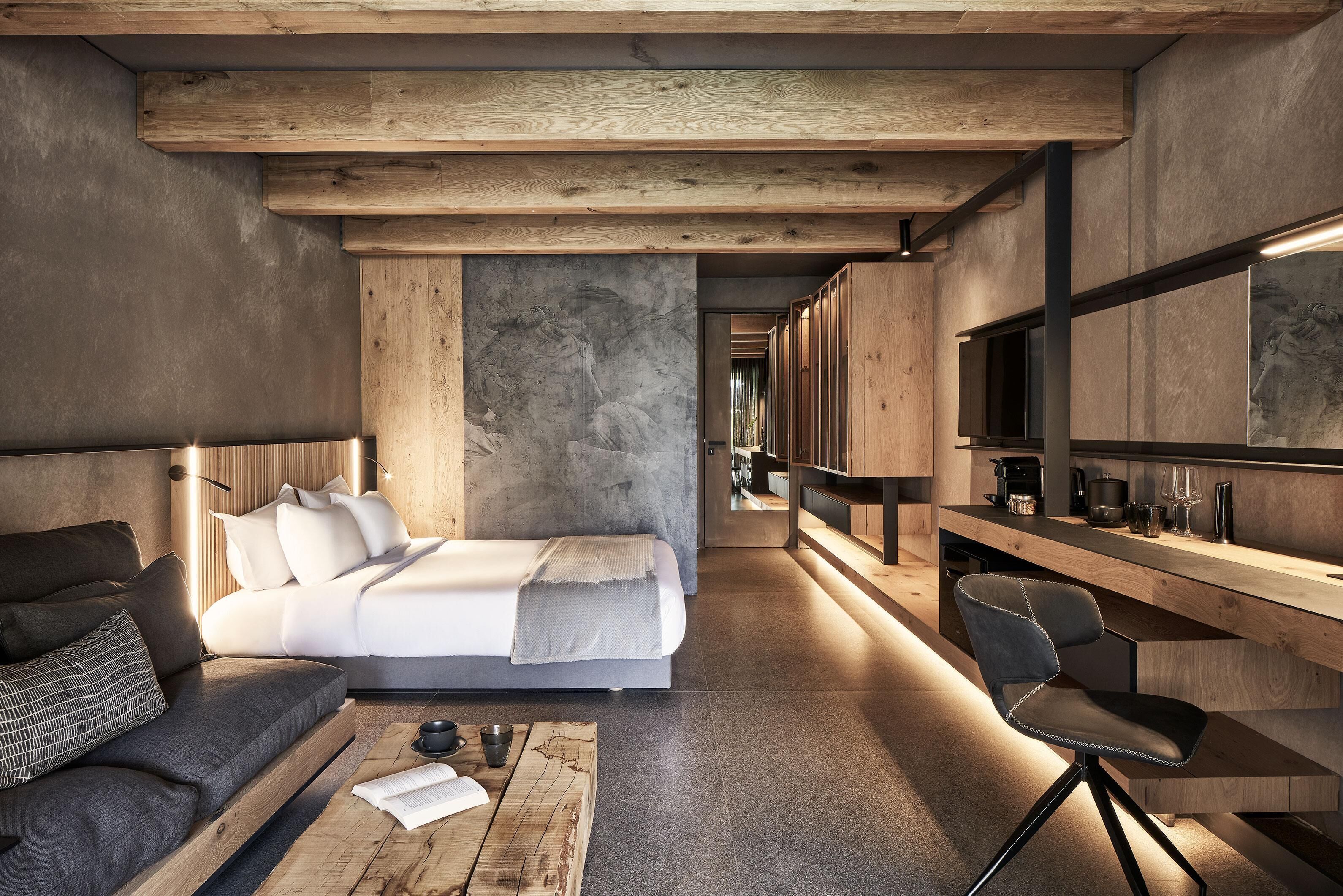 A modern bedroom with a large bed, a wooden bench, a small table, and a chair.