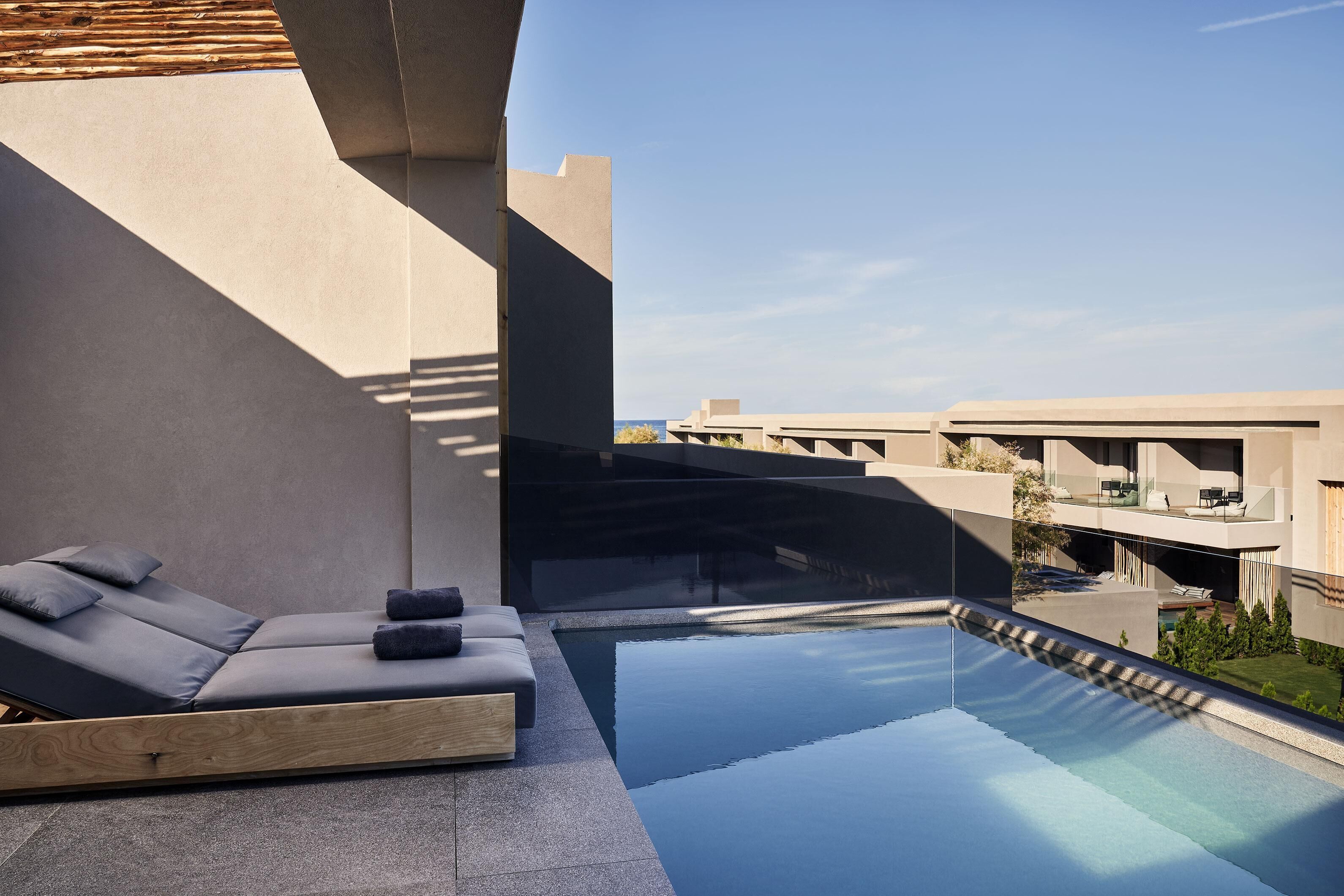 A modern outdoor pool area with a lounge chair and a glass barrier.