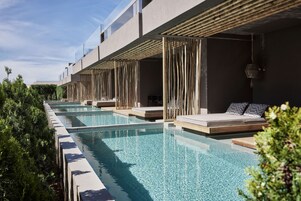 A modern hotel with a long swimming pool, wooden deck, and outdoor seating areas.