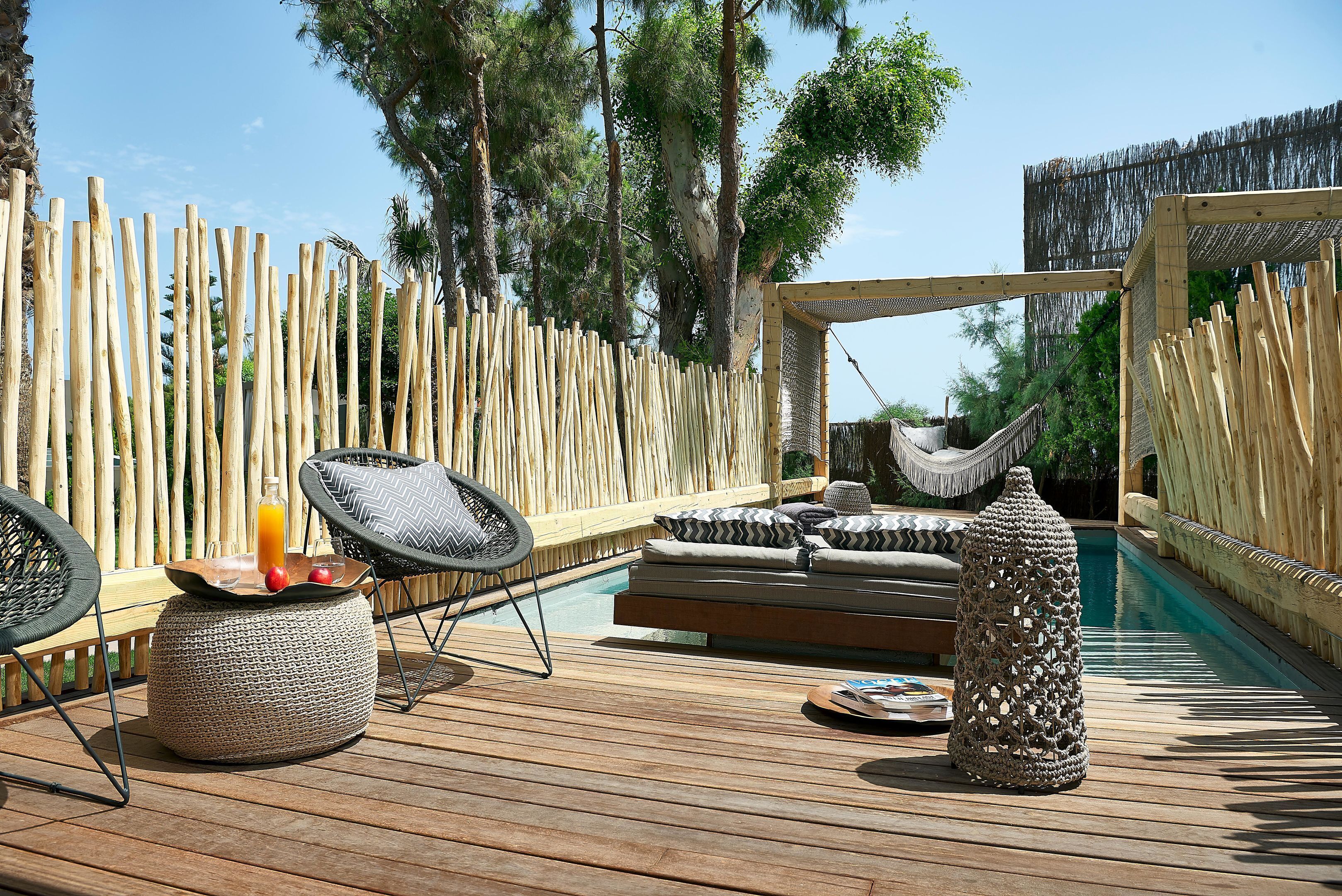 A wooden deck with outdoor furniture, including chairs and a sofa, near a pool area.