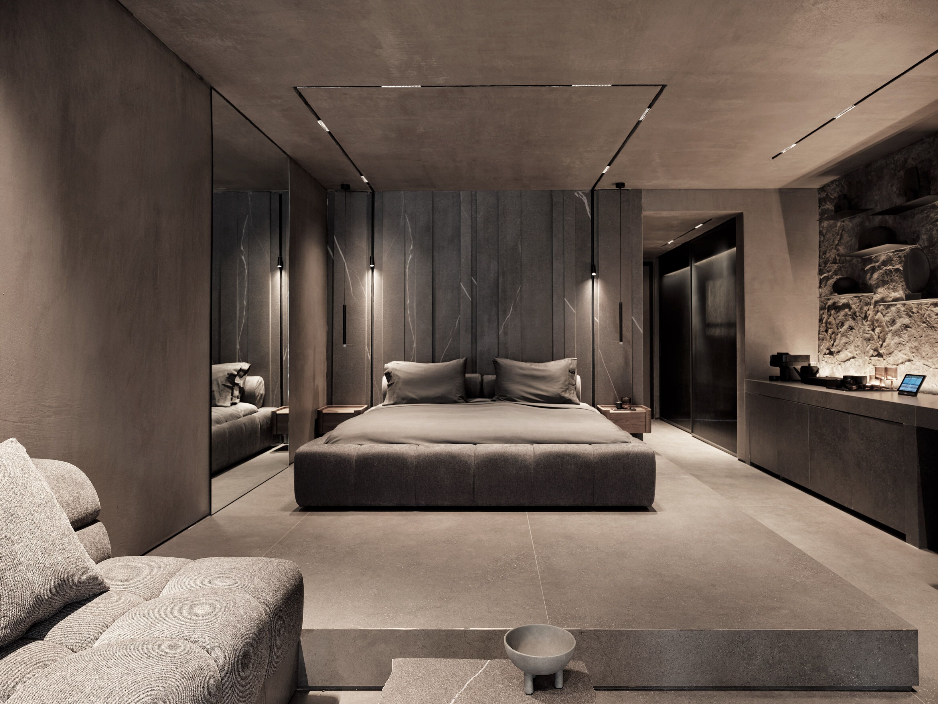 A modern bedroom with a large bed, a seating area, and a built-in desk.