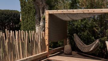 Un área de piscina con terraza de madera, una hamaca y un árbol grande.