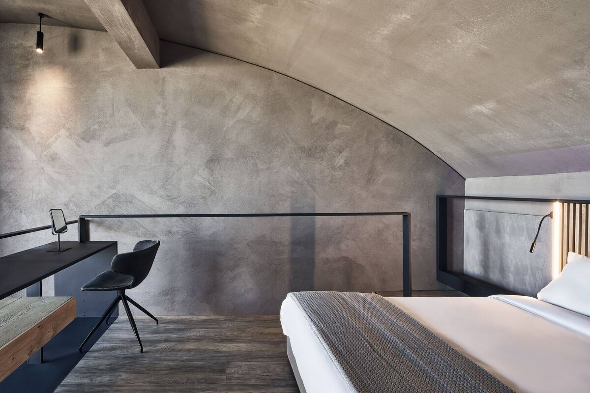A modern bedroom with a curved ceiling, a bed, a desk with a chair, and a hanging light fixture.