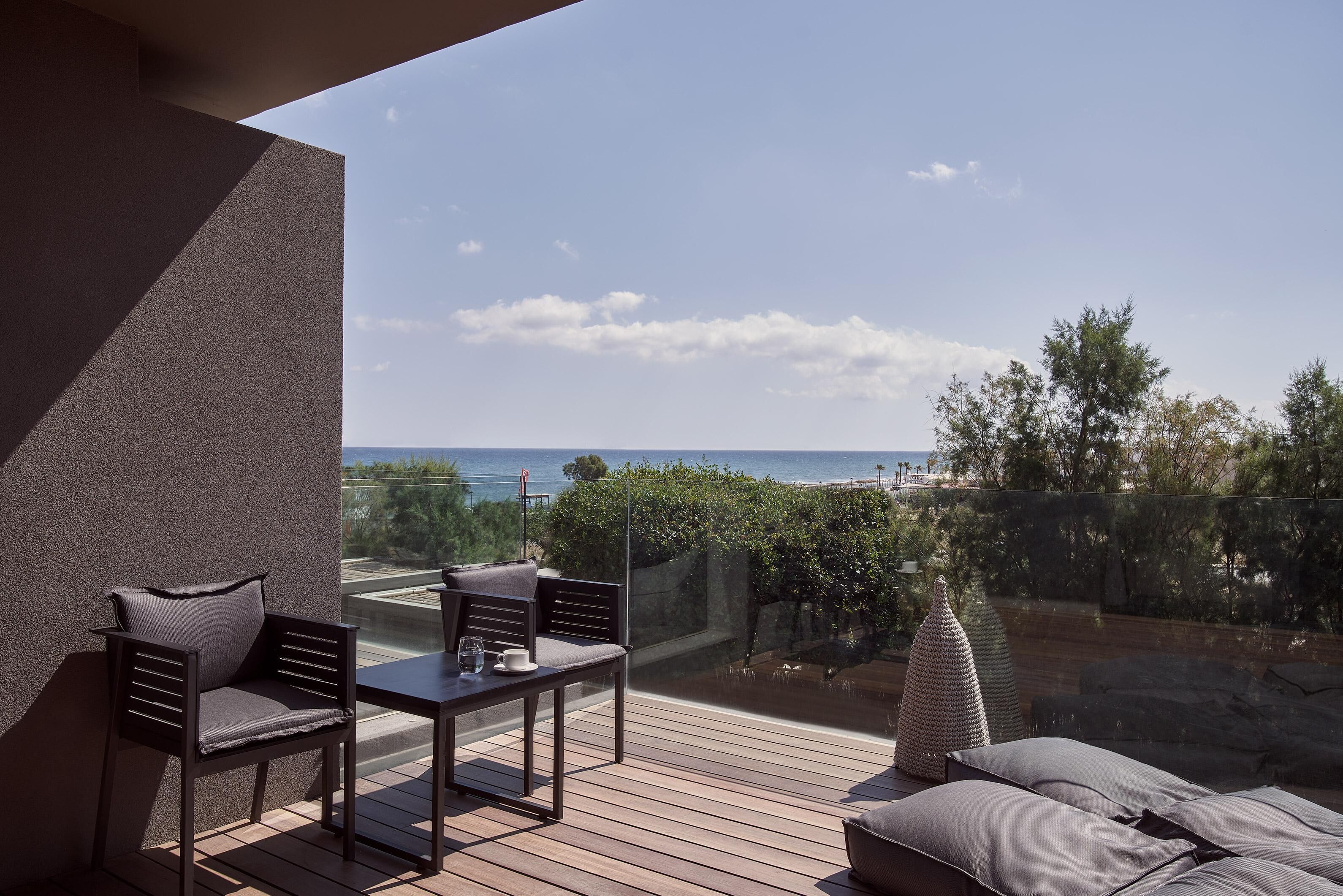 Un balcón con mesa y sillas, vista al mar y un muro de piedra.