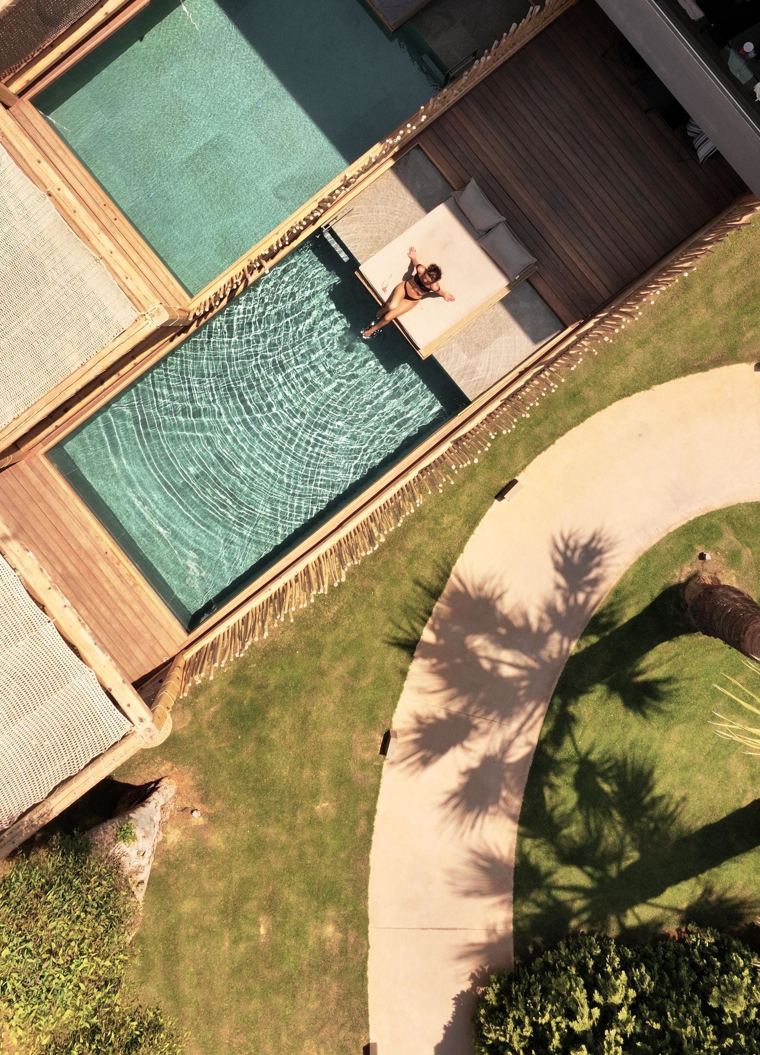 An aerial view of a pool area with a wooden deck, a lounge chair, and a small pool.