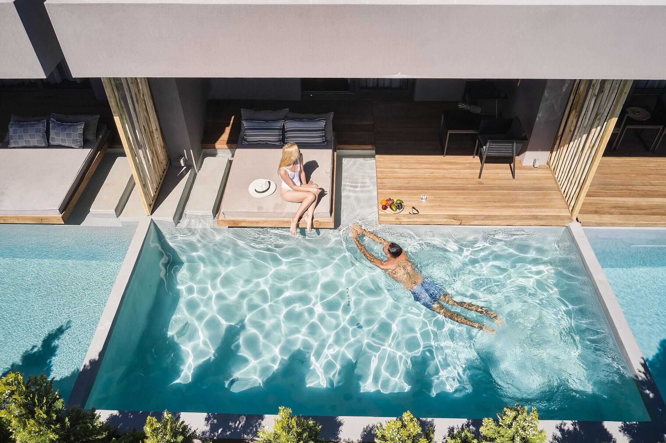 Zona de piscina en la azotea con una persona nadando y otra relajándose en una cama solárium.