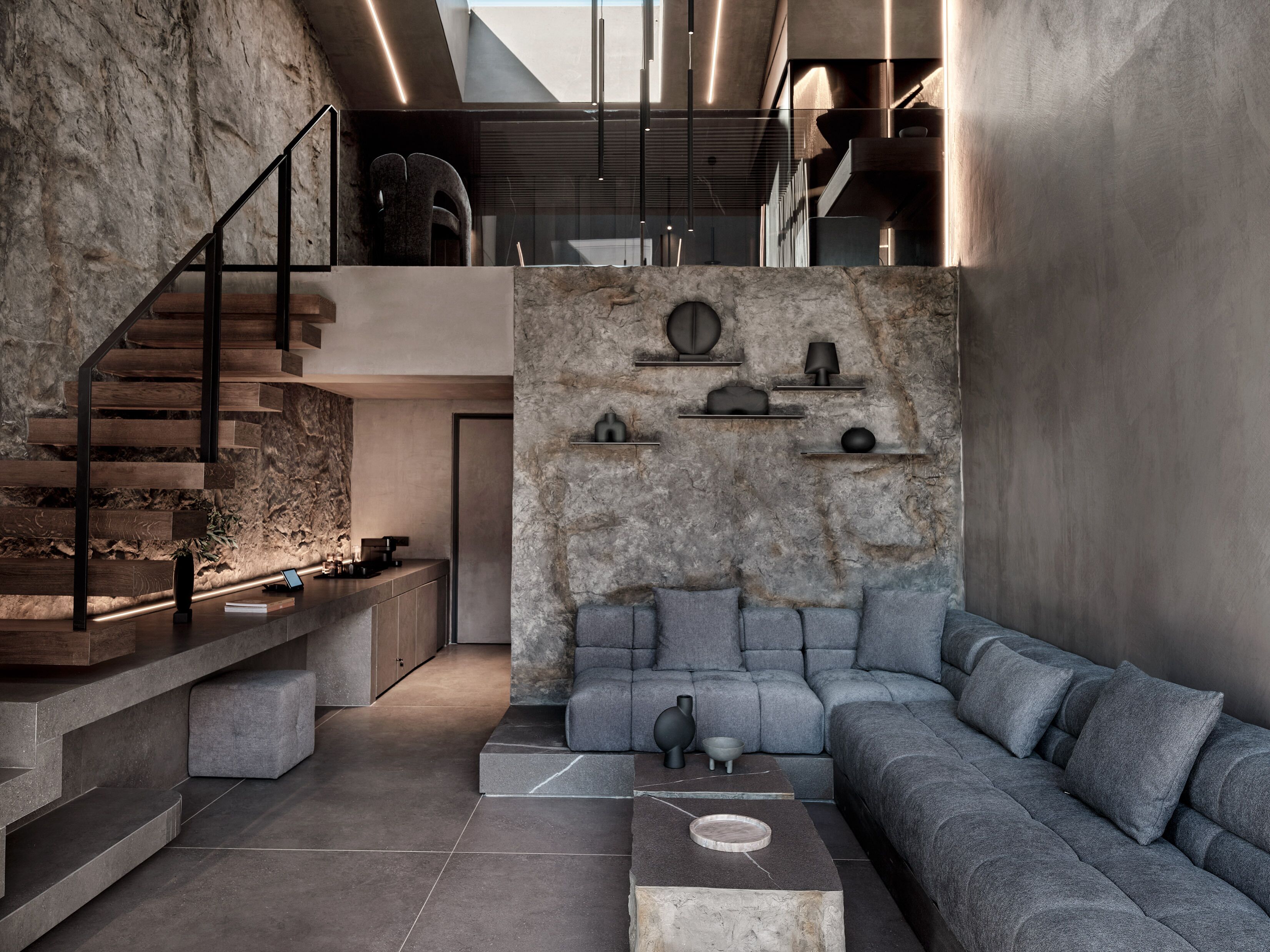 Un interior moderno con una escalera, un sofá modular y una pared de piedra.