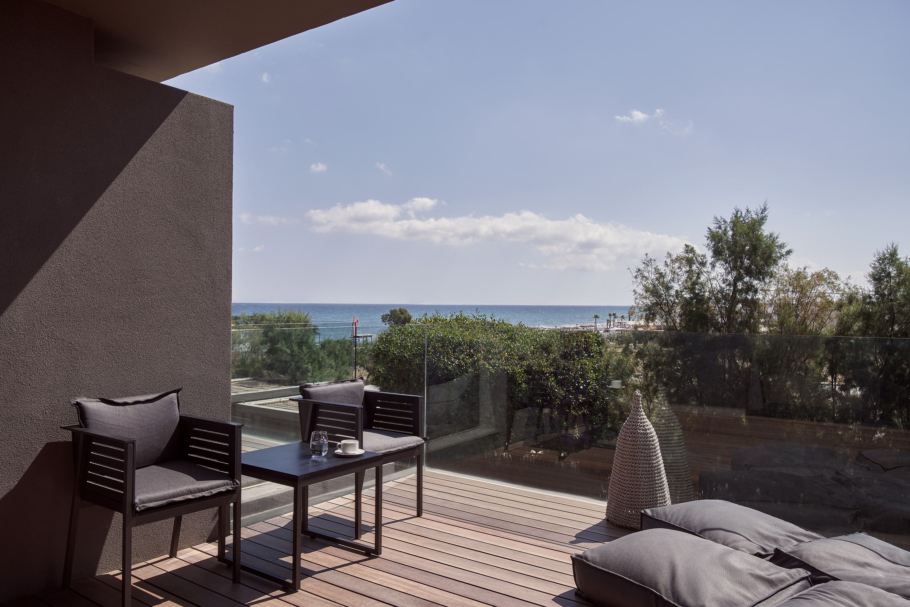 Un balcón con mesa y sillas, vista al mar y un muro de piedra.