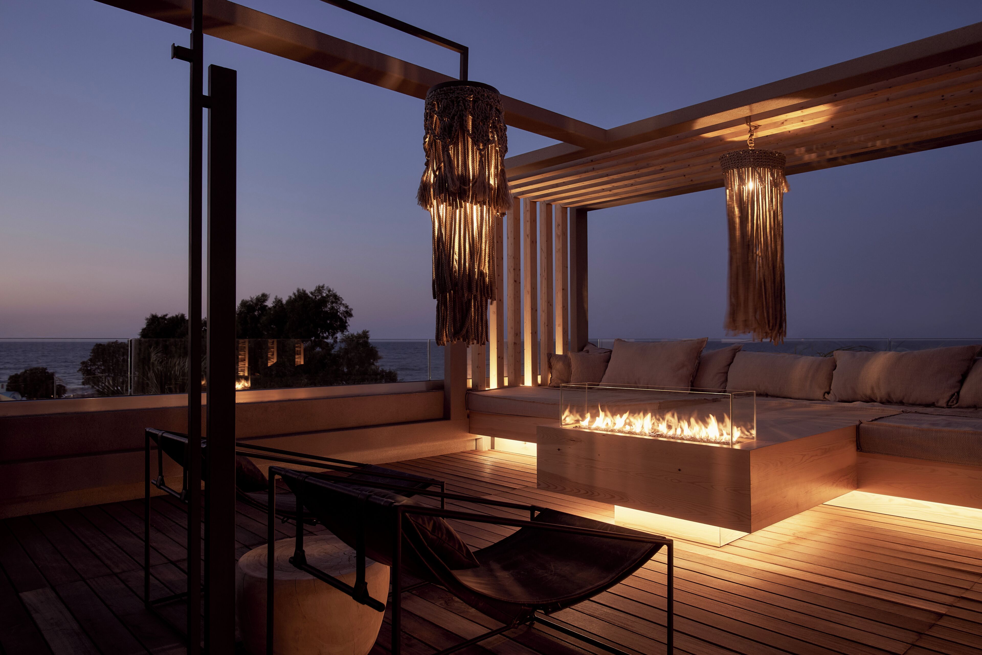 Un área de estar moderna al aire libre con una chimenea, terraza de madera y vistas al océano.