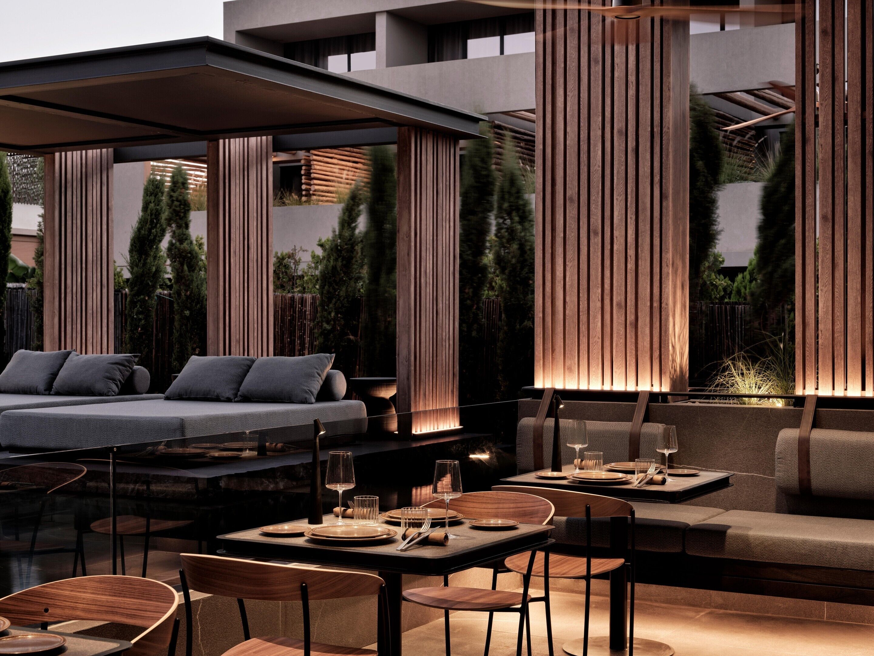 An outdoor dining area with a modern design, featuring a sofa, tables, and chairs.