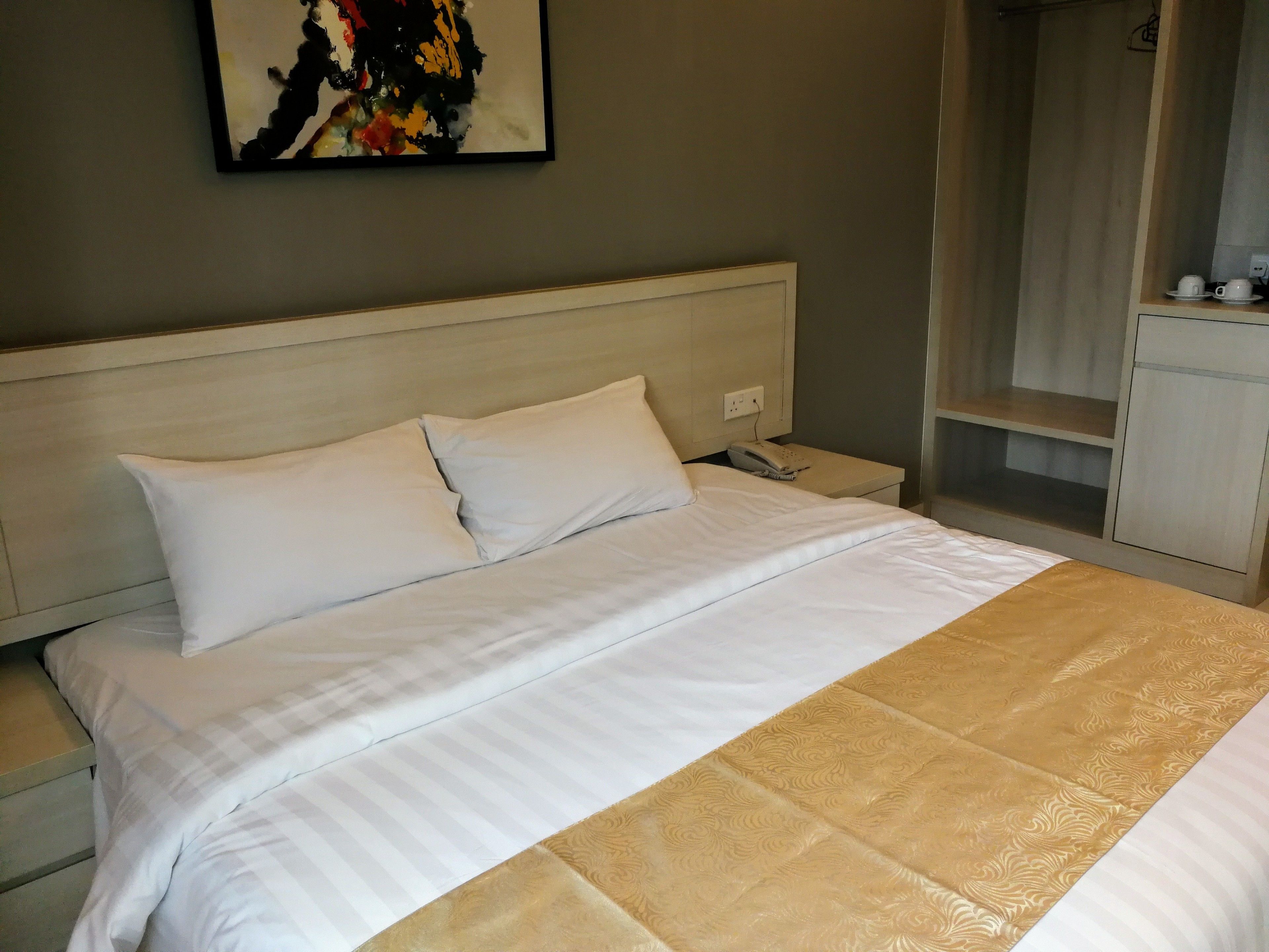 A hotel room with a bed, a nightstand, a telephone, and a small table with cups.