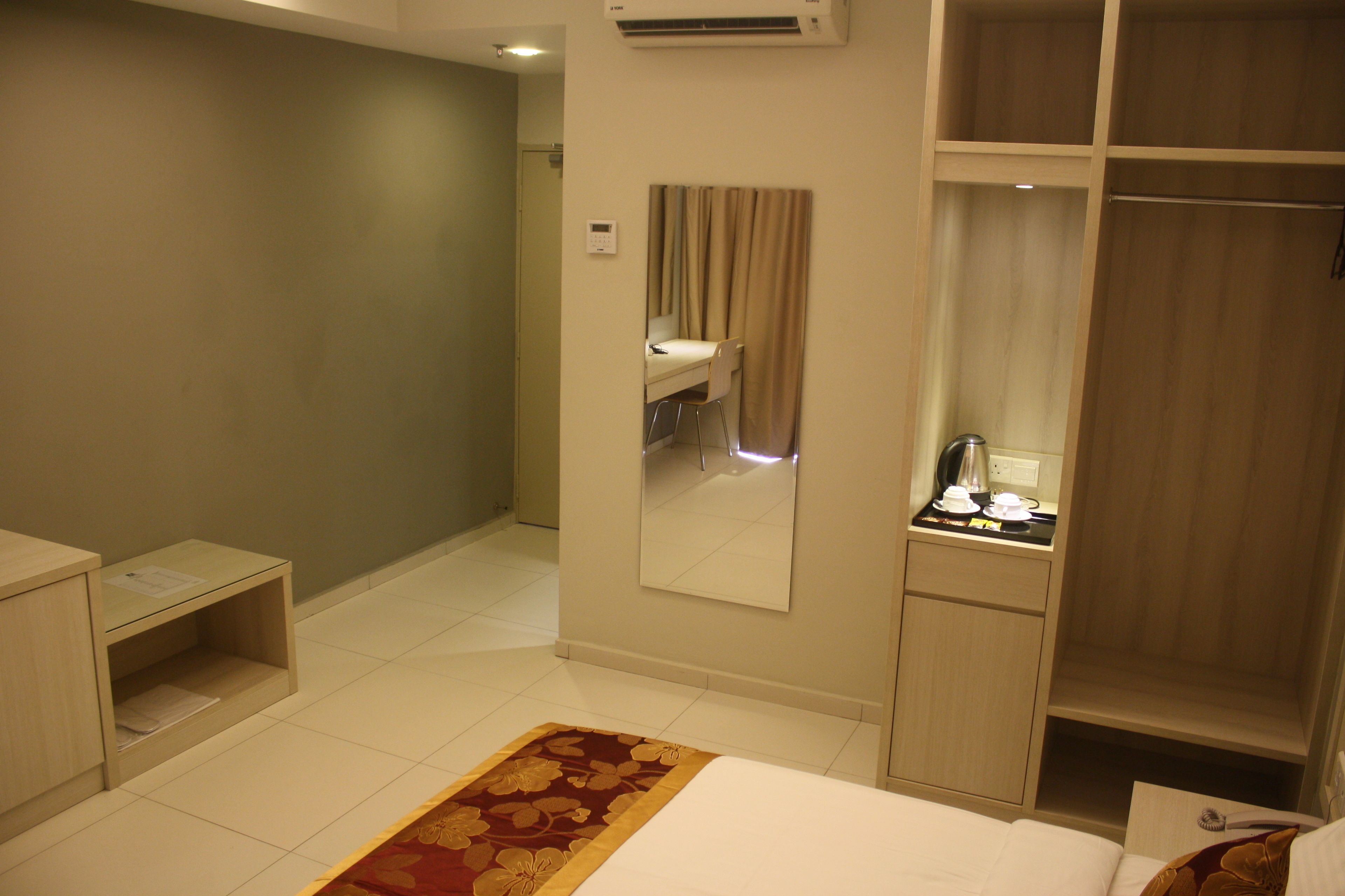 A hotel room with a bed, a bedside table, a mirror, a wardrobe, and a small desk with a chair.