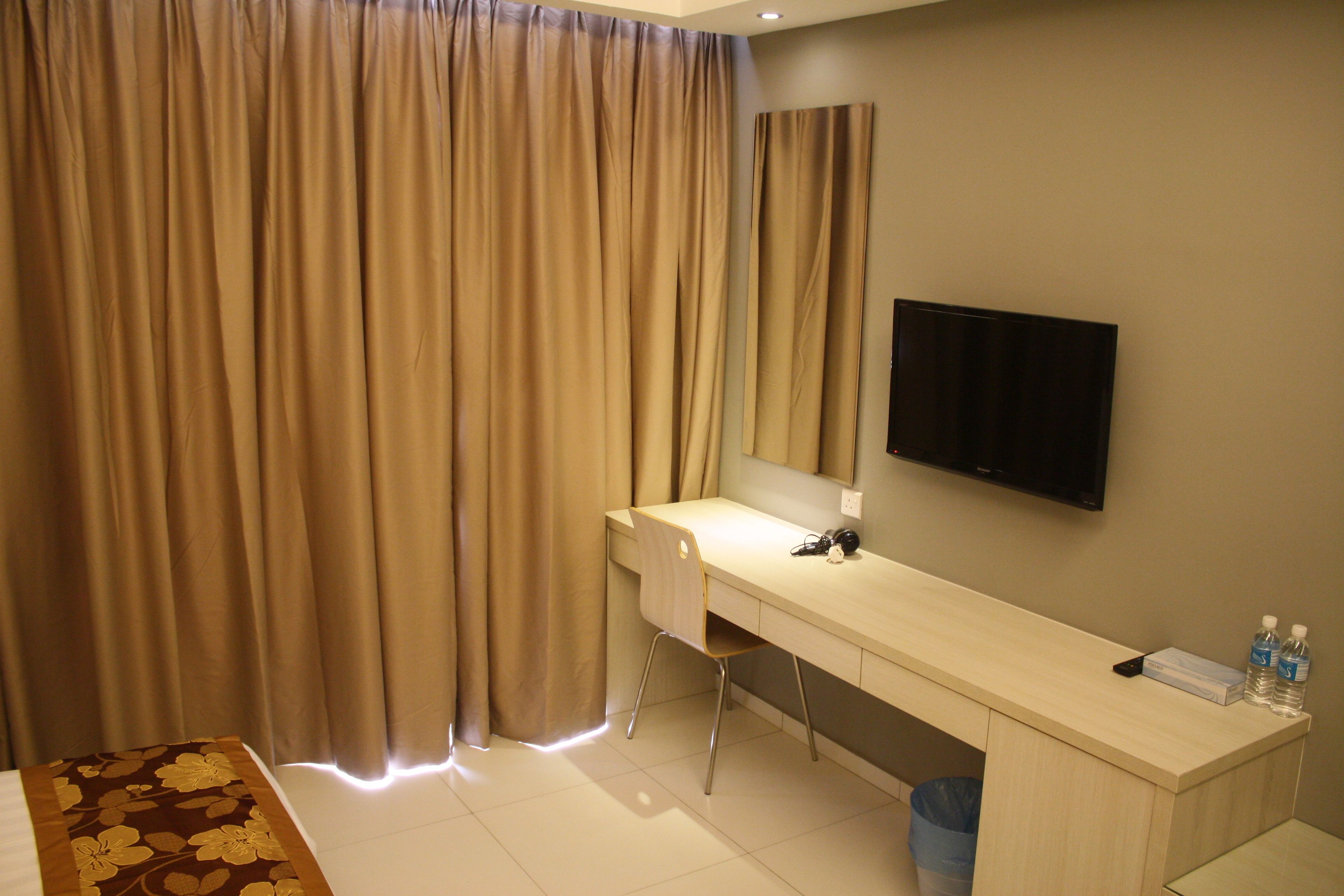 Une chambre d’hôtel équipée d’un bureau, d’une chaise, d’une télévision et de rideaux.