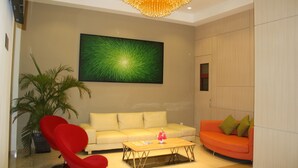 Una sala de estar moderna con un sofá amarillo, un sillón rojo, una mesa de centro de madera y un cuadro abstracto verde de gran tamaño en la pared.