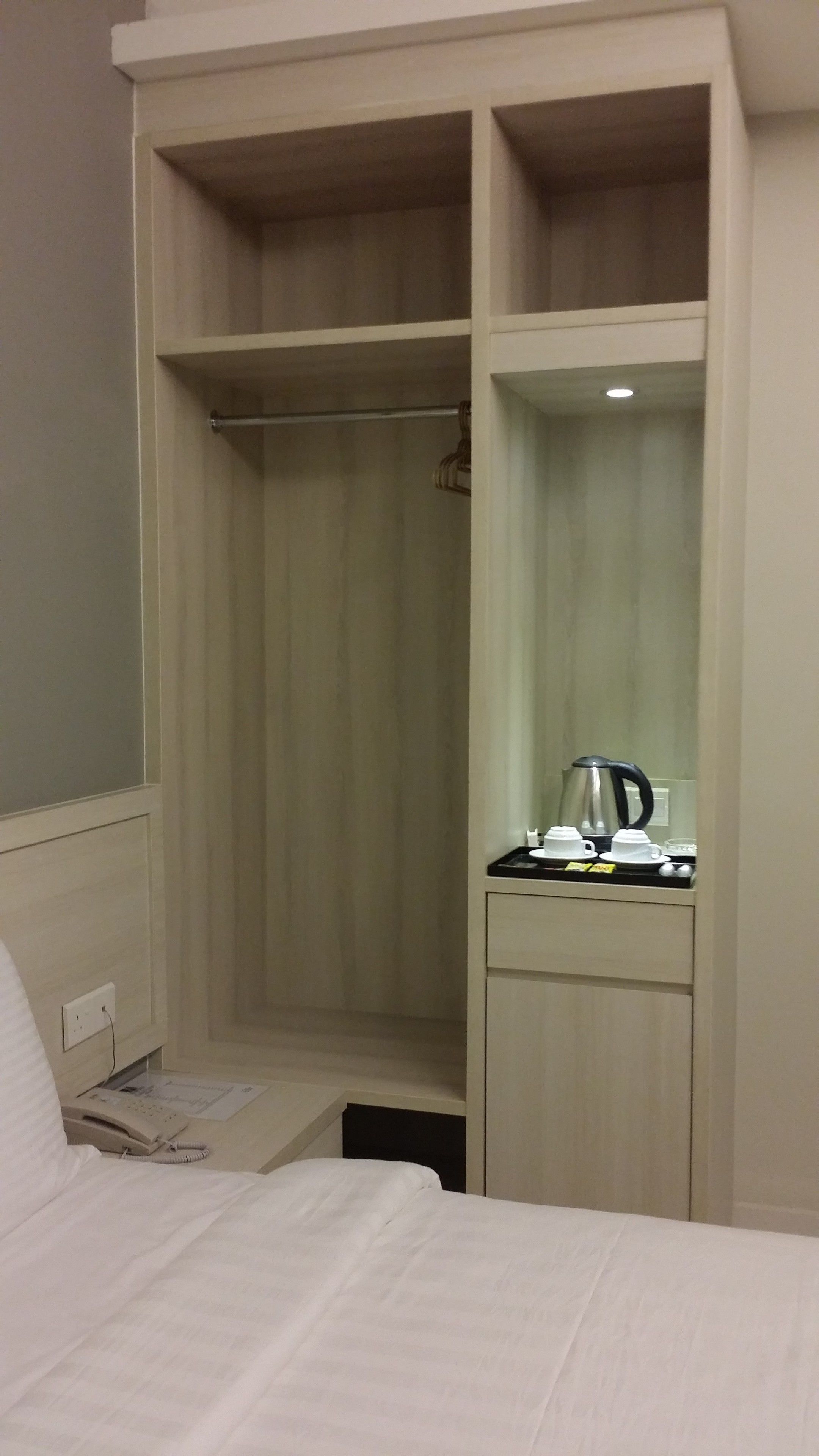 Una habitación de hotel con una cama, un escritorio con hervidor, un teléfono y un espejo.