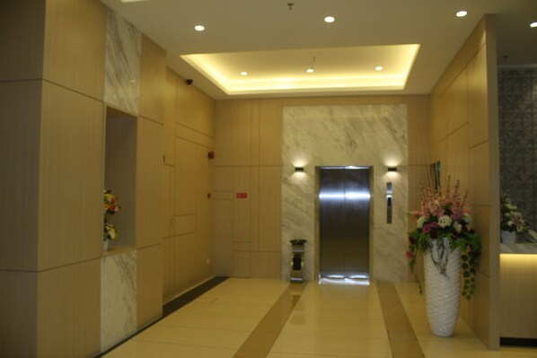 Um hall de hotel moderno com uma recepção de mármore, um vaso grande de flores e um elevador.