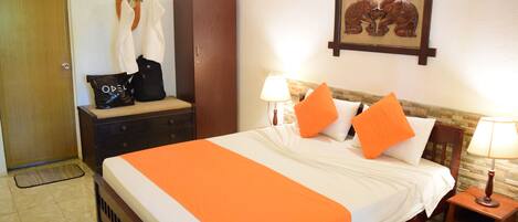 Habitación de hotel con cama, armario de madera, perchero con cabeza de venado, cuadro enmarco con dos gatos y una mesita con lámpara.
