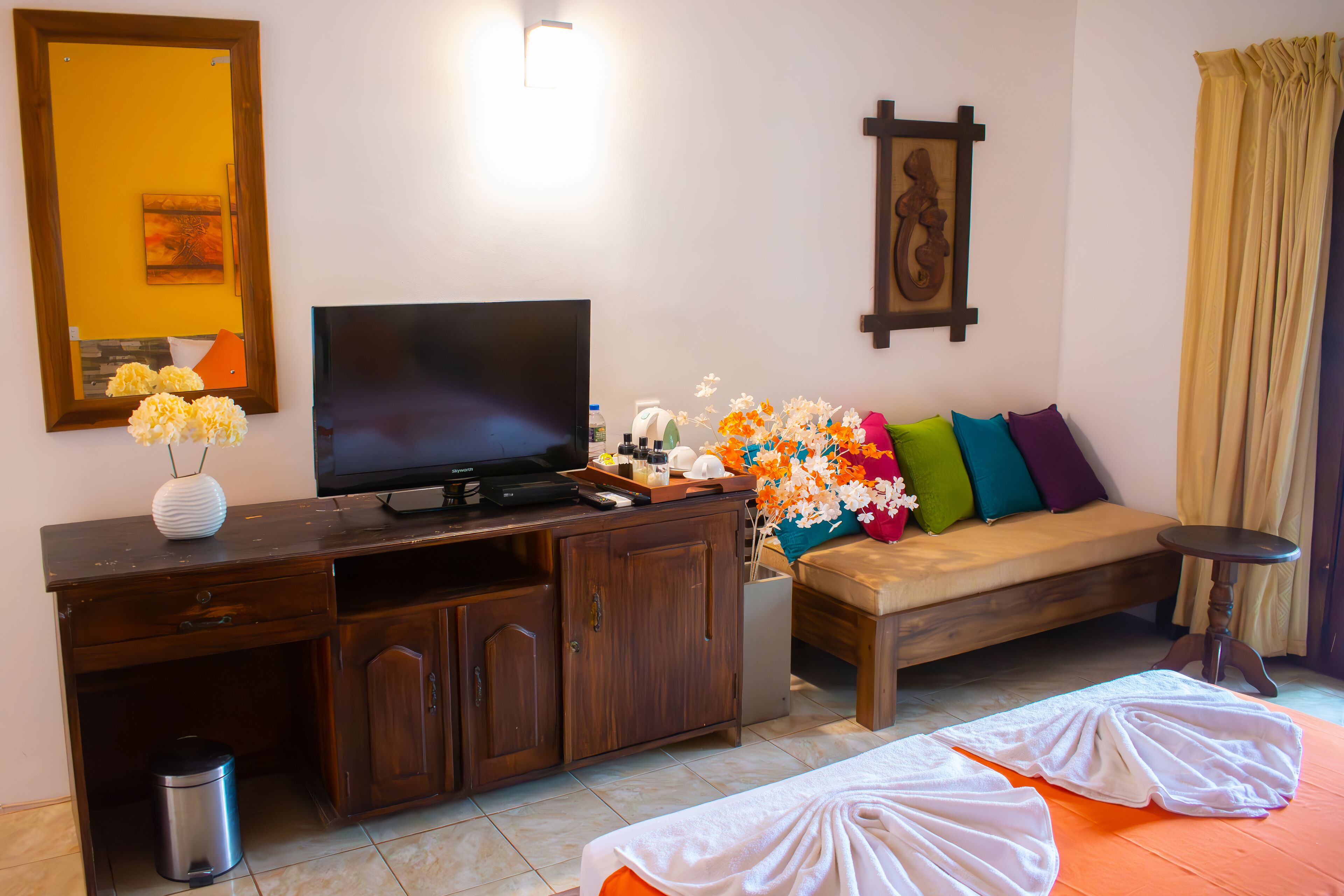 Un salón con televisor, muebles de madera, un sofá con cojines de colores y una mesita.