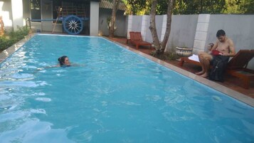 Ein Schwimmbad mit einer Person, die schwimmt, einer Liege und einer Person, die am Beckenrand sitzt.