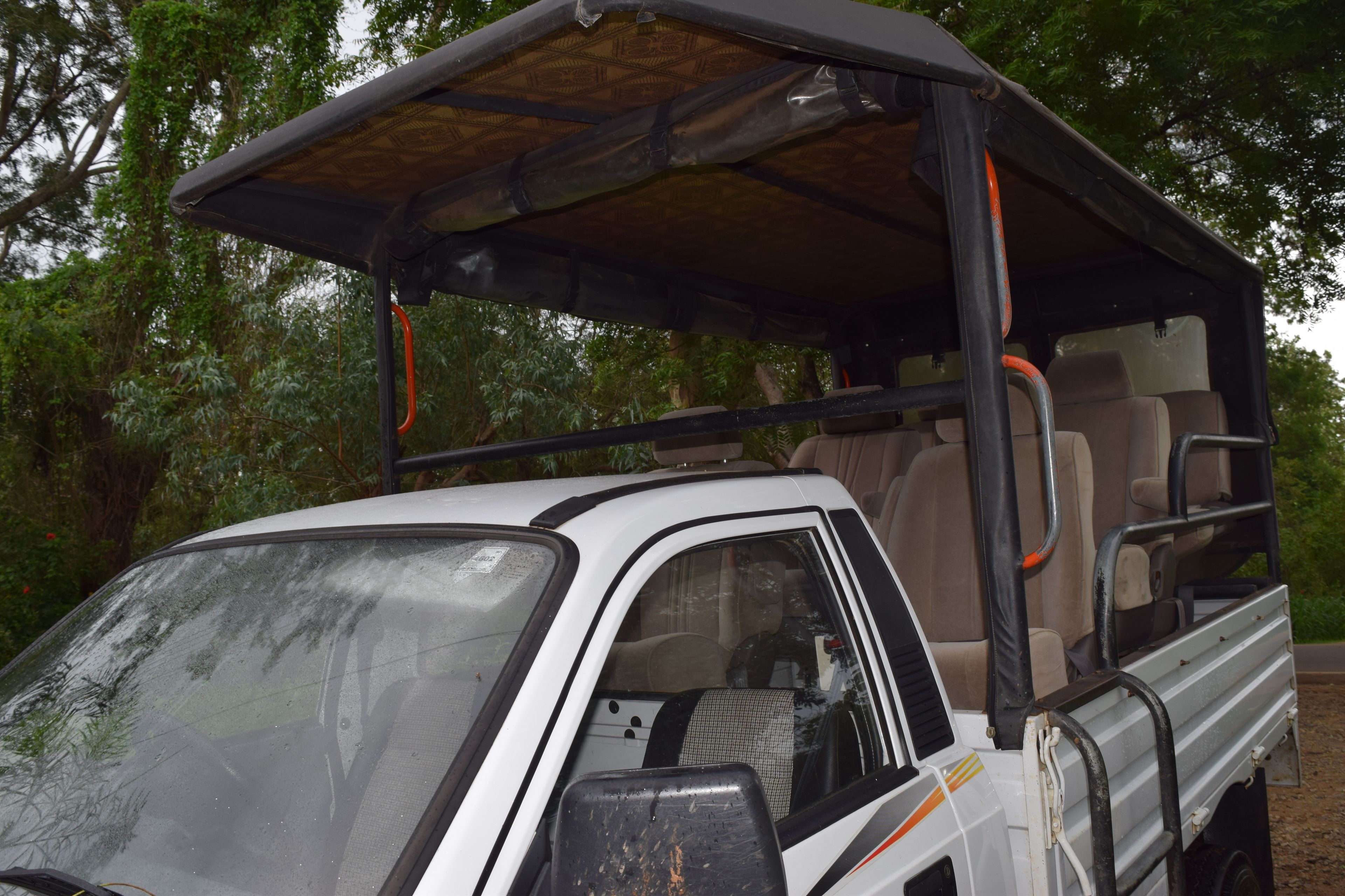 A white safari vehicle with a roof and side steps, equipped with a bench seat and a spare tire mounted on the side.
