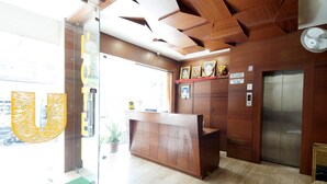 A reception desk with a wooden finish, a security camera, and a service charge sign. - Uddhav Vilas (Udaipur)