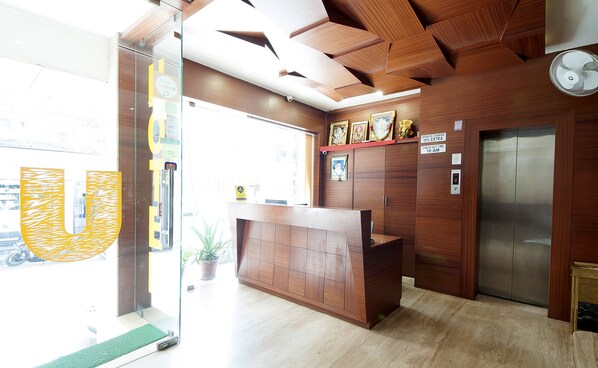 A reception desk with a wooden finish, a security camera, and a service charge sign. - Uddhav Vilas (Udaipur)