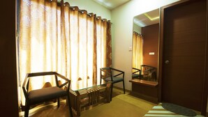 A room with a glass table, two chairs, a mirror, and a wooden door. - Uddhav Vilas (Udaipur)