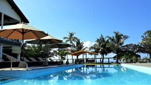 A pool area with lounge chairs and umbrellas, surrounded by palm trees and a clear sky. - Imagine Villa Hotel (Kamburugamuwa)