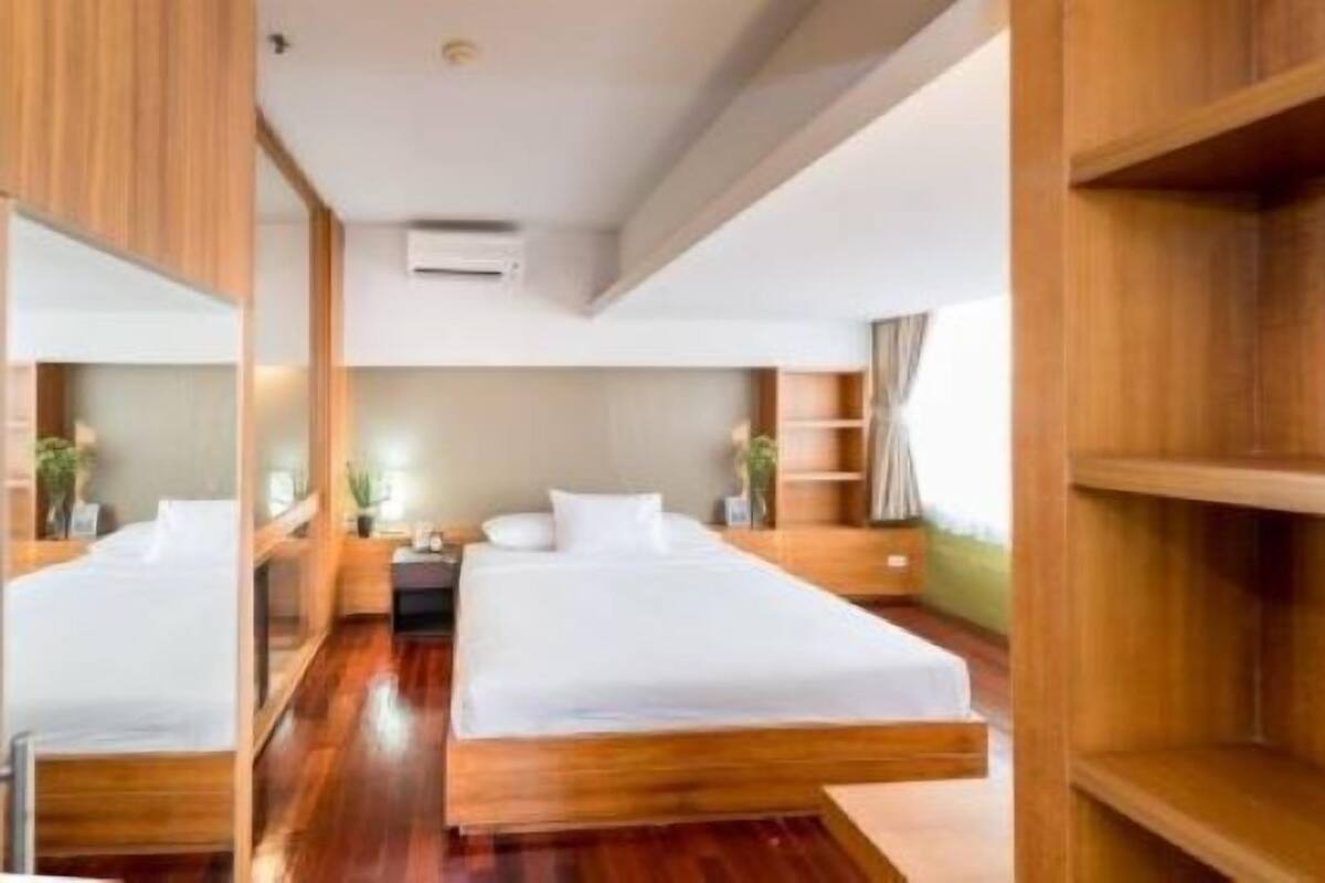 A modern hotel room with a large bed, wooden flooring, and built-in shelving.
