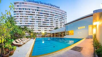 Un hôtel doté d’une piscine, de chaises longues et d’un grand bâtiment portant l’enseigne « Laemtong Serviced Apartment ».