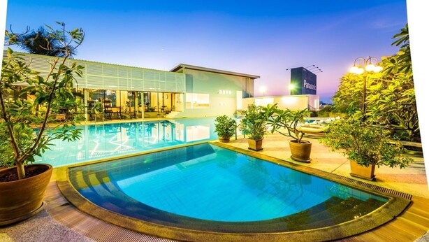 A swimming pool with a tiled deck, surrounded by potted plants and a building with a sign that reads "Panasonic". - Laemtong Service Apartment (Si Racha)