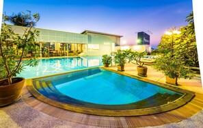 A swimming pool with a tiled deck, surrounded by potted plants and a building with a sign that reads "Panasonic". - Laemtong Service Apartment (Si Racha)