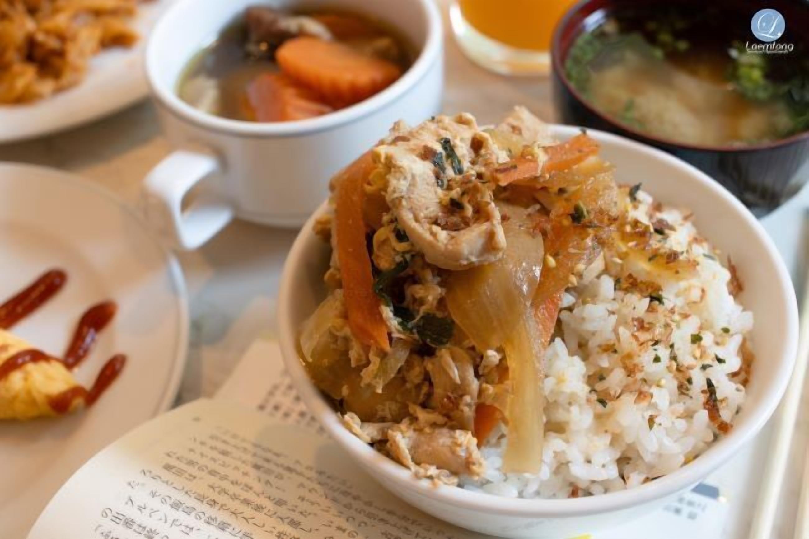 Un tazón de arroz con verduras y carne, una taza de sopa y un vaso de té sobre una mesa con un menú.