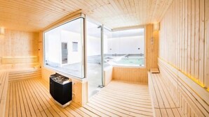 A sauna room with wooden walls and floor, a large window, and a sauna heater. - Laemtong Service Apartment (Si Racha)