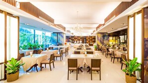 A spacious, modern dining area with multiple tables and chairs, large windows offering views of greenery, and a clean, well-lit interior. - Laemtong Service Apartment (Si Racha)