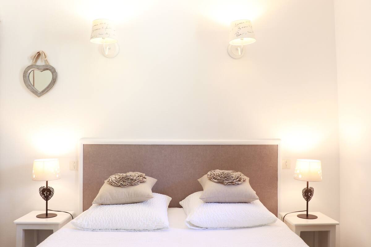 A neatly arranged bedroom with a large bed, two bedside tables with lamps, and decorative wall sconces.