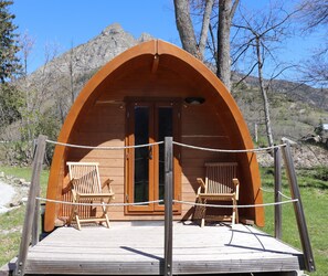 Una cabaña de madera con techo curvo, dos sillas de madera afuera y una barandilla de cuerda.
