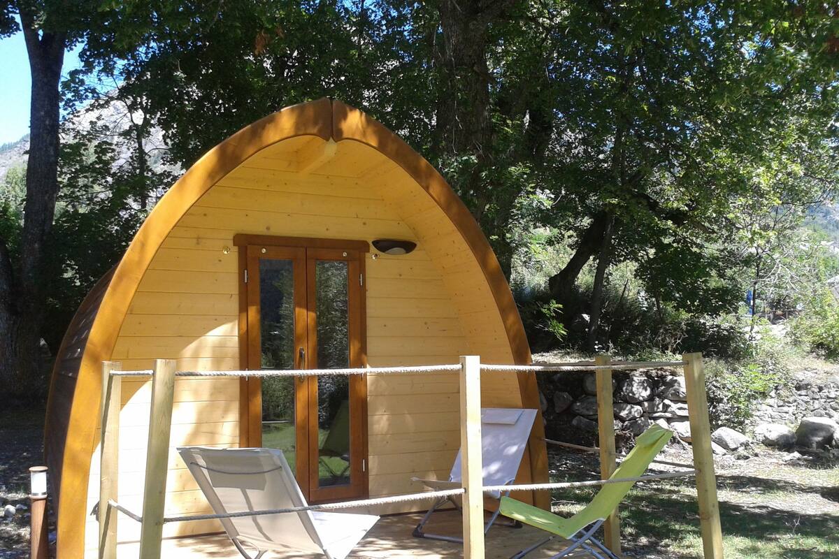 A wooden cabin with a curved roof, two folding chairs, and a rope barrier.