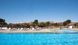 A swimming pool with lounge chairs and umbrellas, surrounded by a landscaped area with trees and a view of a hilltop town. - La Molinera Bungalows (Arcos de la Frontera)