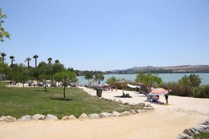 A beach with people, umbrellas, and a lake in the background. - La Molinera Bungalows (Arcos de la Frontera)