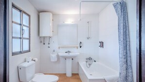 Et badeværelse med toilet, vask, badekar og et vindue.