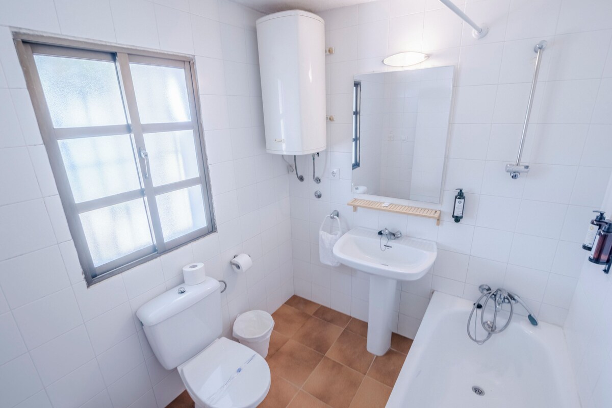 A bathroom with a toilet, sink, bathtub, and a window.
