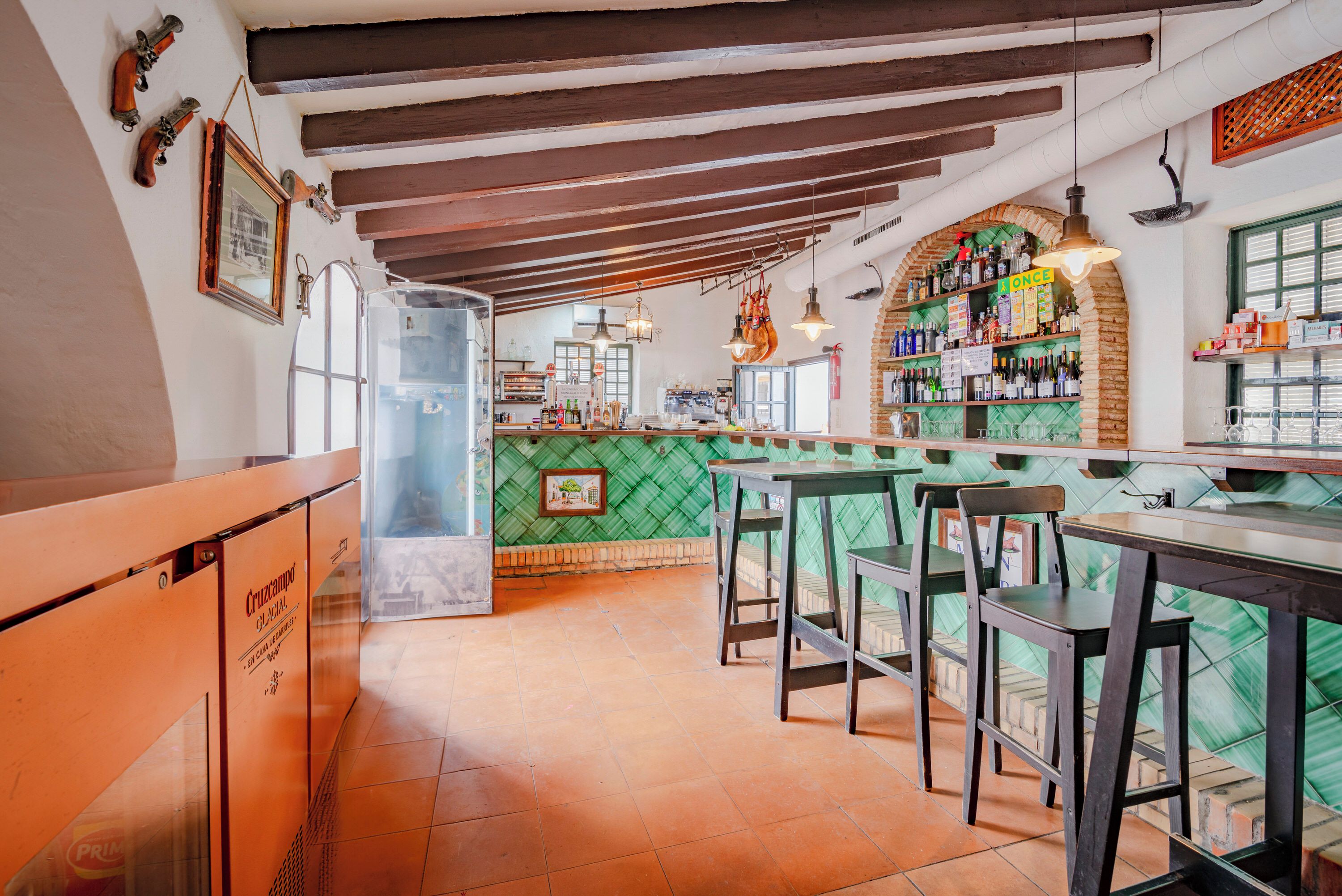 Een restaurantinterieur met een bar, houten balken aan het plafond en een groene tegelwand.